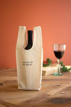 a wine bottle in a bag sitting on a table next to a glass of wine