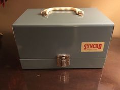 an old style metal tool box sitting on top of a wooden table next to a wall