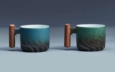 two coffee mugs with wooden handles are sitting side by side on a gray background