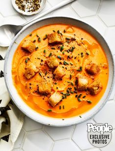 a bowl of soup with croutons and garnishes on the side