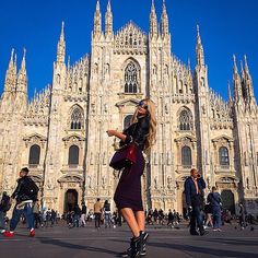 a woman standing in front of a large cathedral looking at her cell phone while people walk by