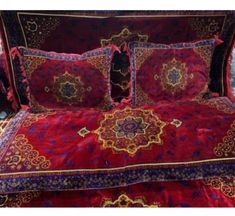 a bed covered in red and purple bedspread with intricately embroidered designs on it