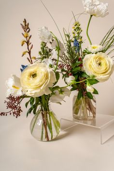 two clear vases with white and yellow flowers in them