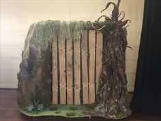 a sculpture made out of wood and grass on top of a wooden floor next to a black curtain