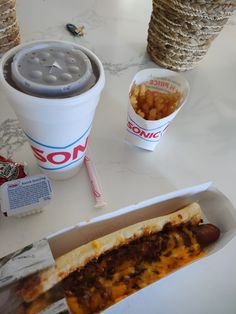 a hot dog in a paper container next to a drink