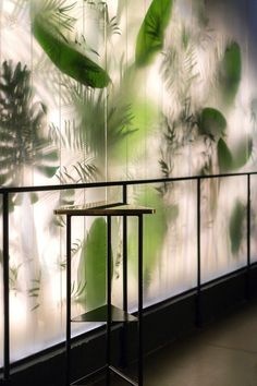 a table sitting in front of a glass wall with plants painted on the walls behind it