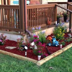 a wooden deck with flowers and toys on it in front of a house that's attached to the porch