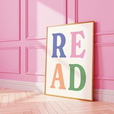 a framed poster with the words read on it in front of a pink wall and wooden floor