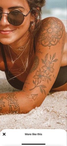 a woman laying on the beach with tattoos on her arm