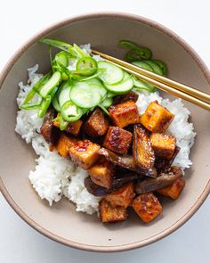 a bowl with rice, cucumbers and tofu on it next to chopsticks