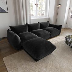 a large black couch sitting on top of a rug in a living room next to a window