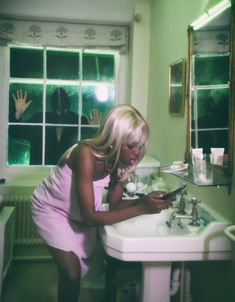 a woman is looking at her cell phone in the bathroom sink while another person looks on