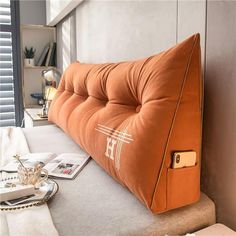 an orange pillow sitting on top of a bed next to a window