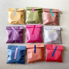 six different colored paper bags with some stickers on them, all lined up in the same row