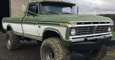 an old green and white truck is parked in front of a building with two large tires