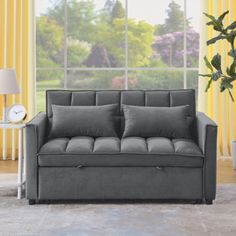 a gray couch sitting in front of a window with yellow drapes on the windowsill