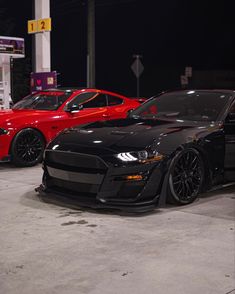 two cars are parked next to each other in a parking lot with gas pumps behind them