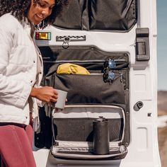 a woman standing next to an open suitcase on the back of a white truck with it's door open