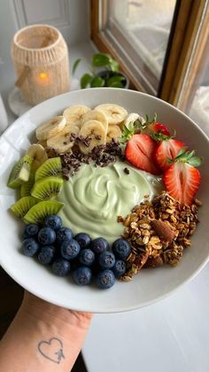 a white plate topped with fruit and yogurt on top of a table next to a window