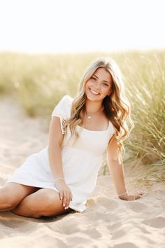 a beautiful blonde woman sitting on top of a sandy beach next to tall green grass