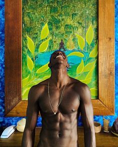 a shirtless man sitting in front of a painting