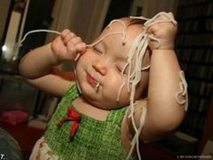 a baby is playing with some white yarn on her head and hands while she holds it up to her face