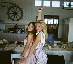 two beautiful young women standing next to each other in front of a table with plates on it