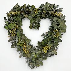 a heart shaped wreath made out of green leaves and yellow flowers on a white background