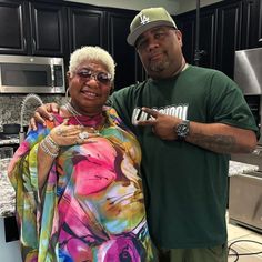 a man standing next to an older woman in a kitchen with black cabinets and counter tops