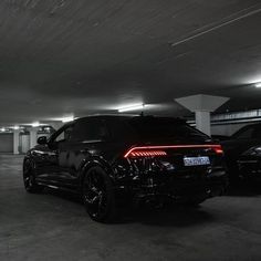 two cars parked in a parking garage with their lights on and one car is black