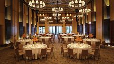 a banquet hall with round tables and chandeliers on the ceiling is lit by lights