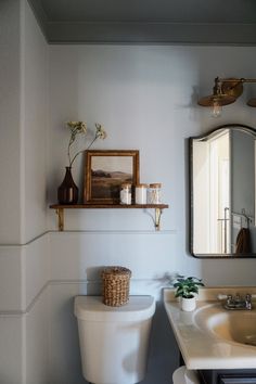 a white toilet sitting next to a bathroom sink under a mirror on top of a wall