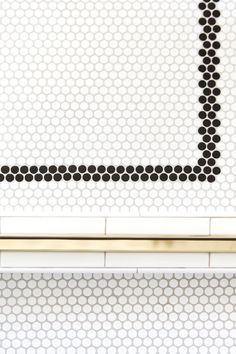 a white tiled bathroom with black dots on the wall and gold trim around the edge