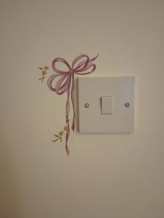 a white light switch with a pink bow on it's side and flowers painted on the wall