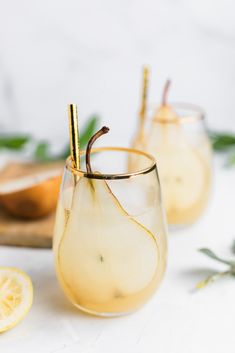 two glasses filled with lemonade sitting on top of a white table next to sliced lemons