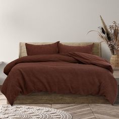 a bed with a brown comforter on top of it next to a vase filled with dried flowers