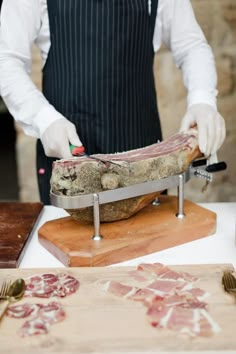 a man in an apron preparing food on a cutting board with knives and tongs