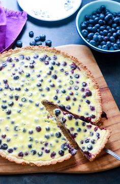 a blueberry cheesecake on a cutting board with a piece missing from the pie