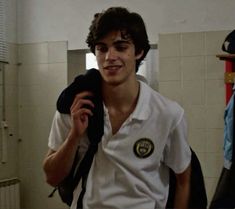 a young man in a white shirt is holding a black backpack and smiling at the camera