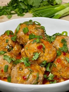 a white bowl filled with meatballs covered in sauce and garnished with cilantro