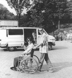 an old black and white photo of two people in a parking lot holding hands with a man in a wheel chair