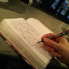 a person holding a pen and writing on an open book with the pages lined in cursive writing