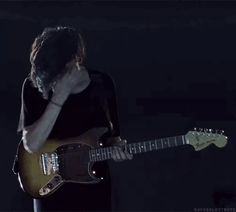 a man holding a guitar in his right hand and looking down at the ground while standing next to him