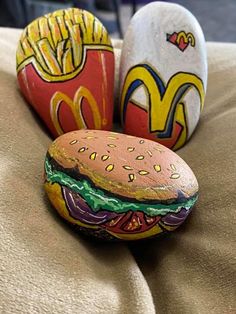 three painted rocks sitting on top of a bed next to each other with mcdonald's logo on them