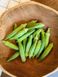 a wooden bowl filled with green beans on top of a table