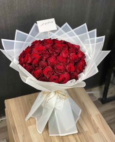 a bouquet of red roses wrapped in white paper on a wooden table with a price tag