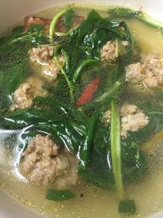 a white bowl filled with meat and spinach in broth sauce on top of a table