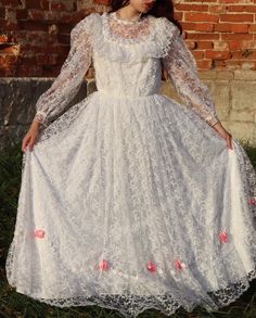 a woman in a white dress is standing by a brick wall