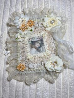 an altered picture frame with flowers and lace on it's edges, sitting on a white bed sheet