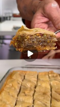 a person holding up a piece of food in front of a pan filled with pastries